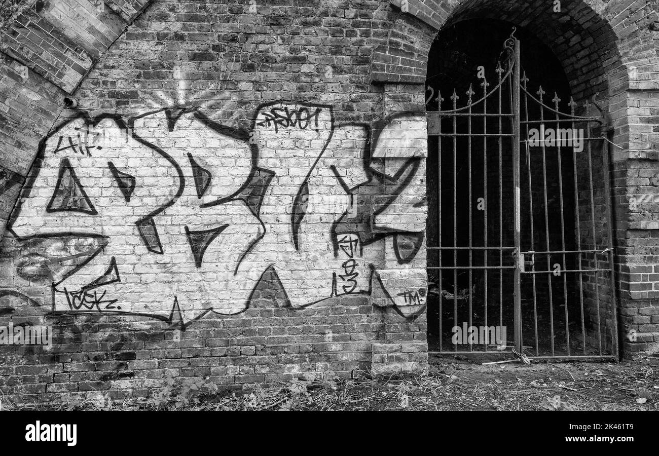 Graffiti an der Wand von einem schmiedeeisernen Tor bemalt, das einen Eisenbahnbogen schützt, London, England in schwarz und weiß Stockfoto