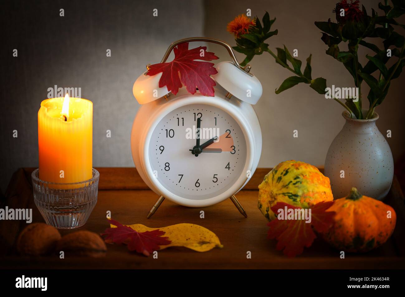 Fallen Sie zurück, ändern Sie die Zeit auf einem weißen Wecker nach der Sommerzeit, Kerze, Blätter und Kürbisse als Herbstdekoration, ausgewählter Fokus Stockfoto