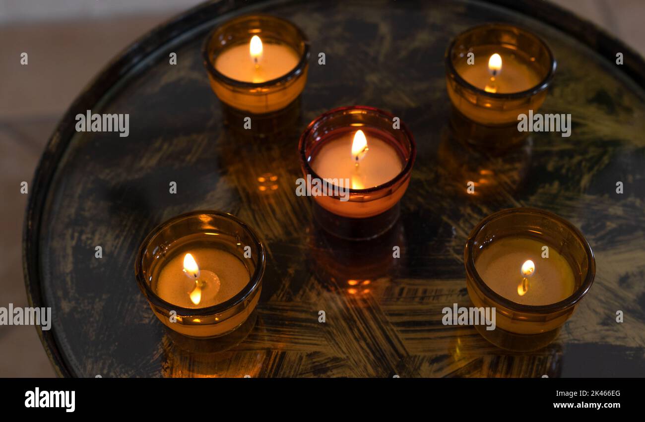 Fünf brennende Votivkerzen in Glasschüsseln auf einem Tablett Stockfoto