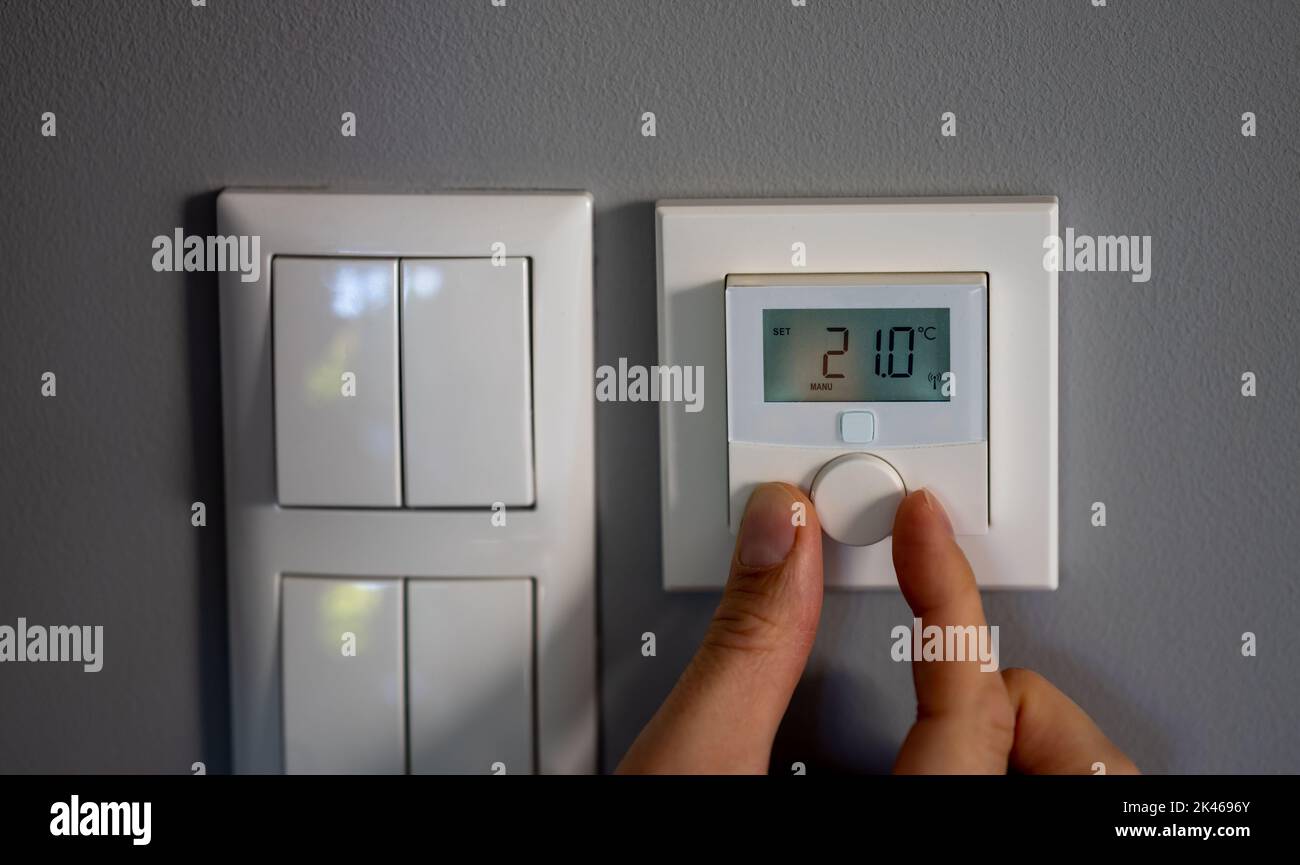 Mit einem elektronischen Thermostat ändert die Hand die Temperatur auf 21 Grad Celsius. Symbol für Energieeinsparung. Stockfoto