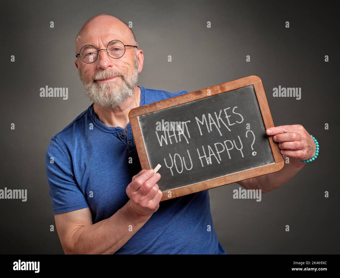 Was macht dich glücklich? Tafel Schild gehalten von einem älteren Mann, Lehrer, Mentor oder Moderator, Glück und persönliche Entwicklung Konzept. Stockfoto
