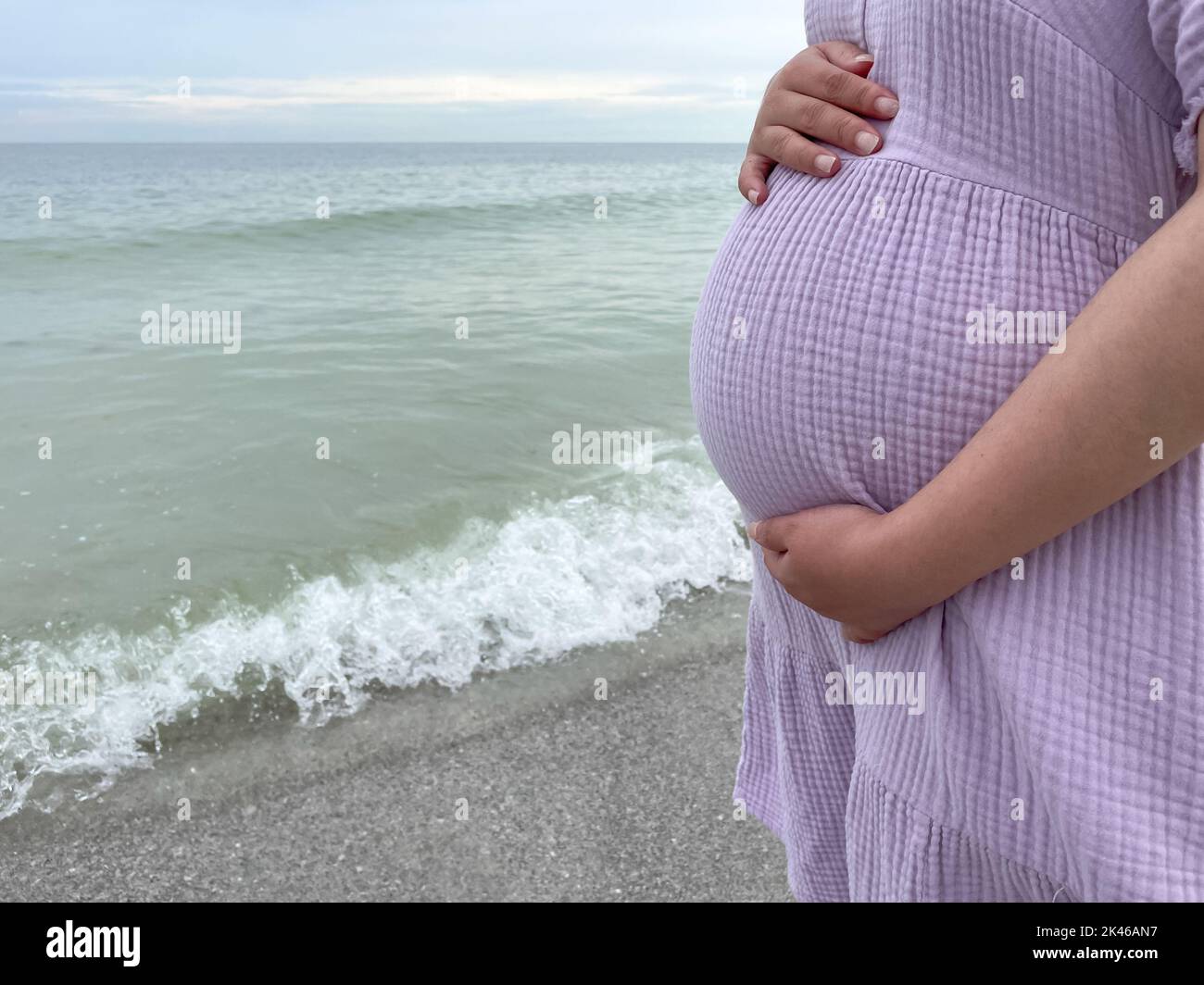 Aufnahme einer Schwangeren, die mit der Hand am Bauch am Strand steht - Schwangerschaft, Erwartung, Mutterschaft Konzept Stockfoto