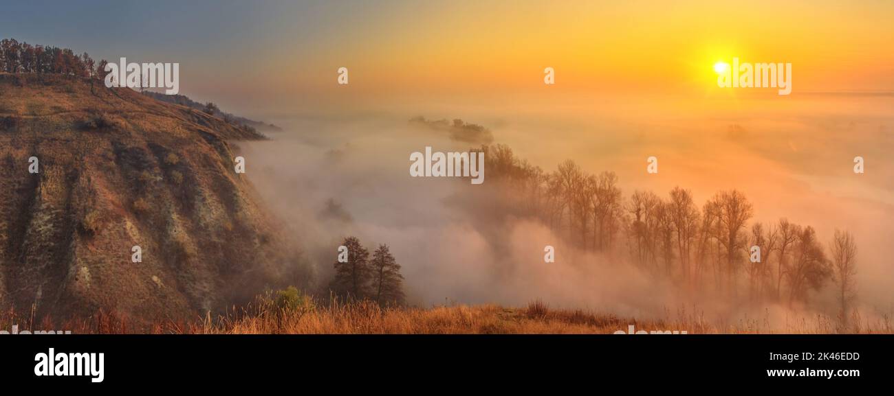 Herbstsonnenaufgangslandschaft, Panorama, Banner - Blick auf ein mit Nebel bedecktes Flusstal im Licht der Sonnenstrahlen, den Nordosten der Ukraine Stockfoto