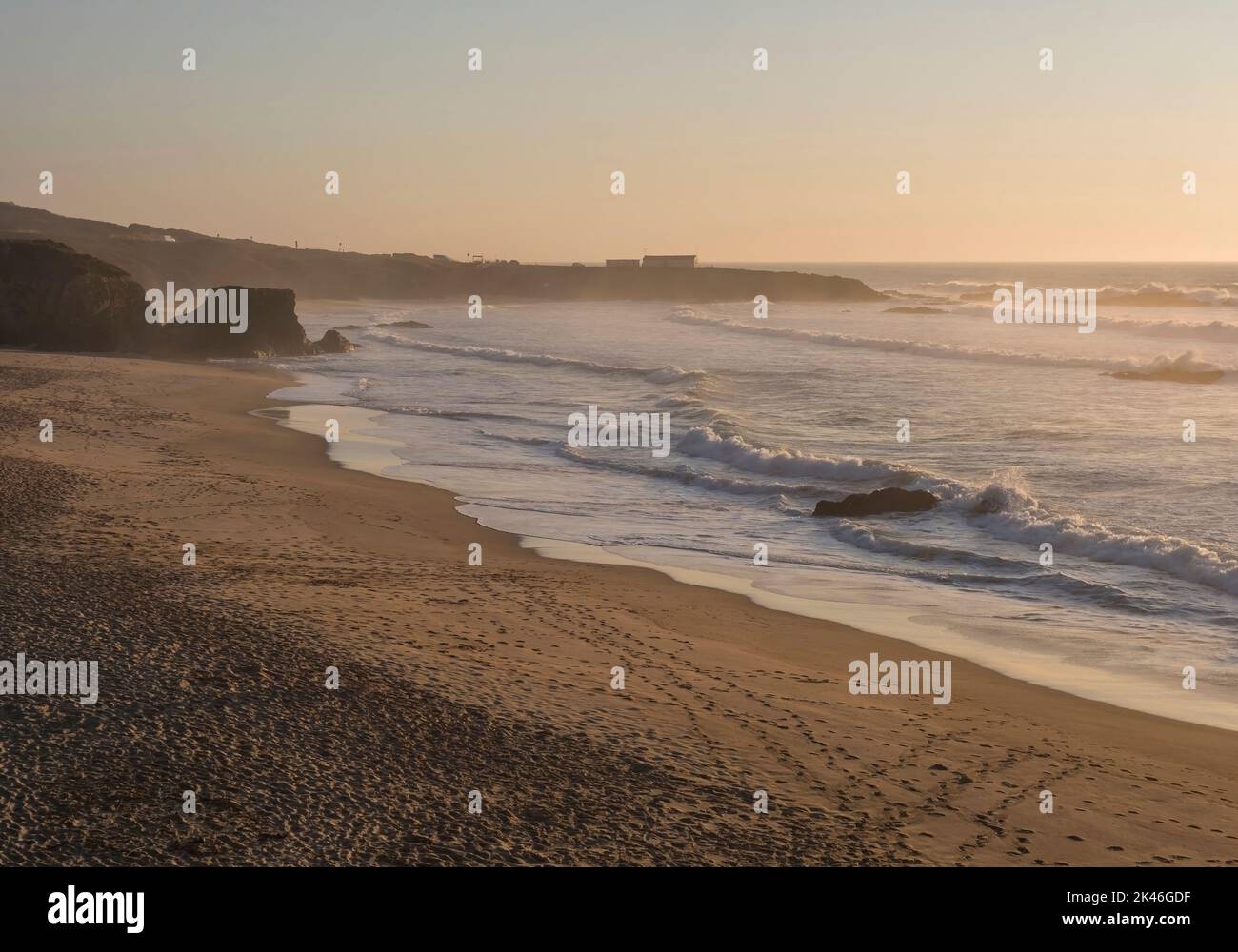 Blick auf den leeren Sandstrand Praia Grande de Almograve mit Meereswellen im goldenen Stundenlicht, klarem blauen Himmel. Küste von Rota Vicentina, Almograve, Portugal Stockfoto