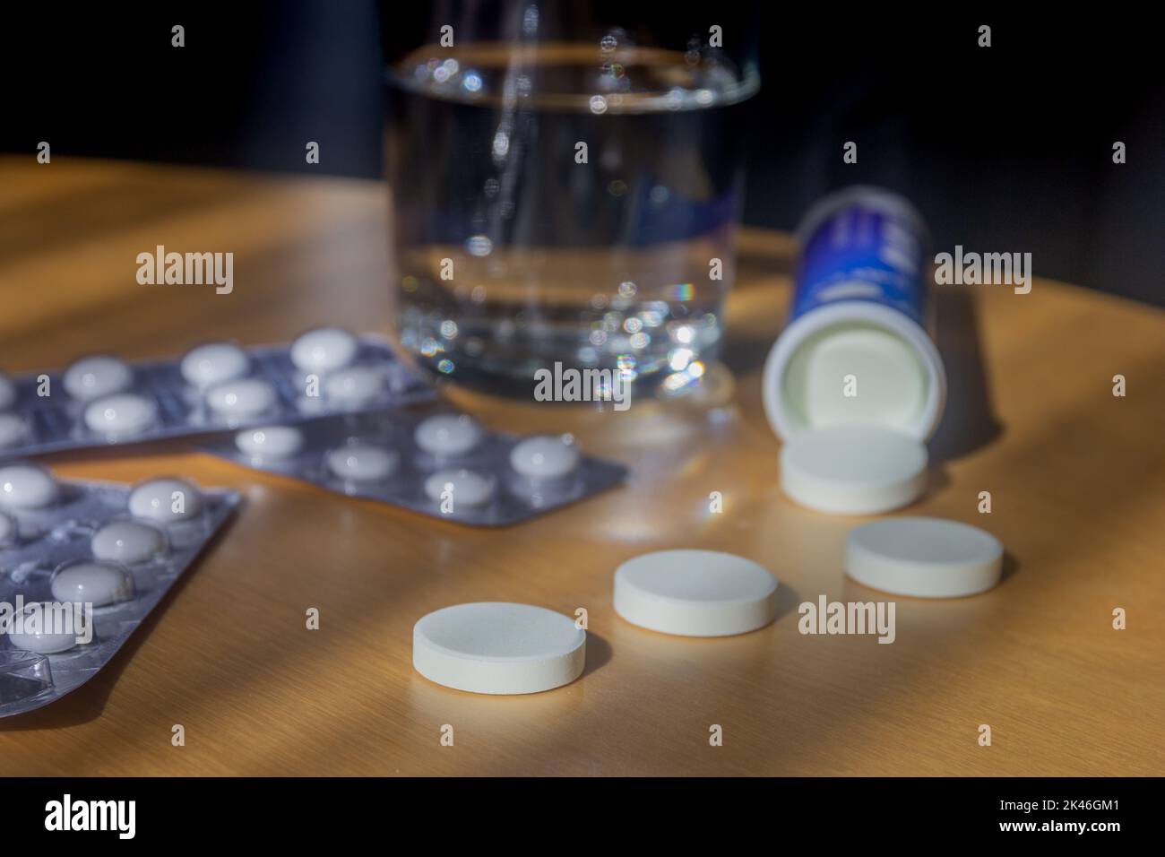 Tabletten und ein Glas Wasser auf einem Holztisch, selektiver Fokus, Medikamente, die aus der Box verschüttet werden Stockfoto