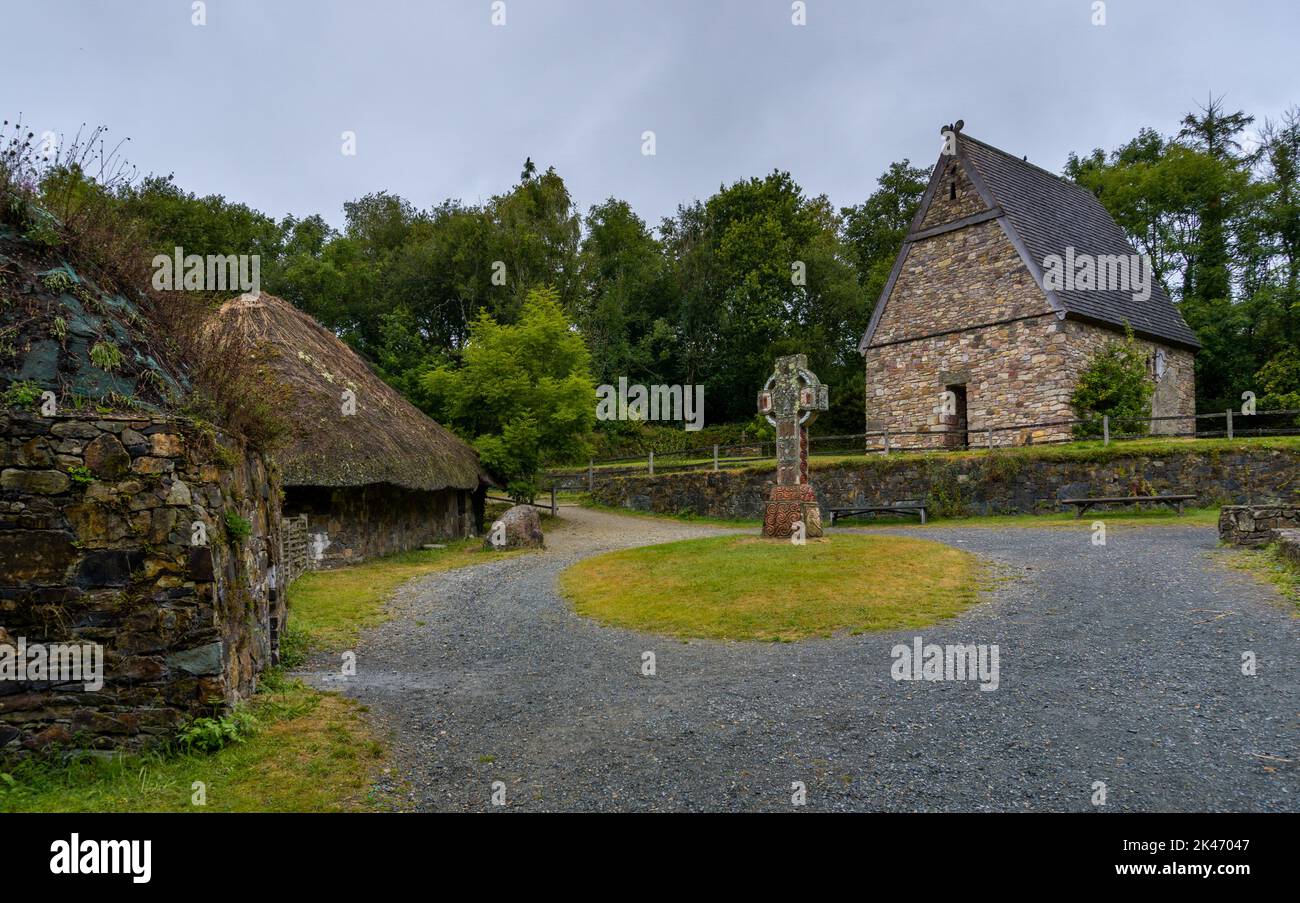 Wexford, Irland - 18. August 2022: Blick auf ein frührekonstruiertes christliches Kloster im Irish National Heritage Park mit einem großen keltischen Kreuz i Stockfoto