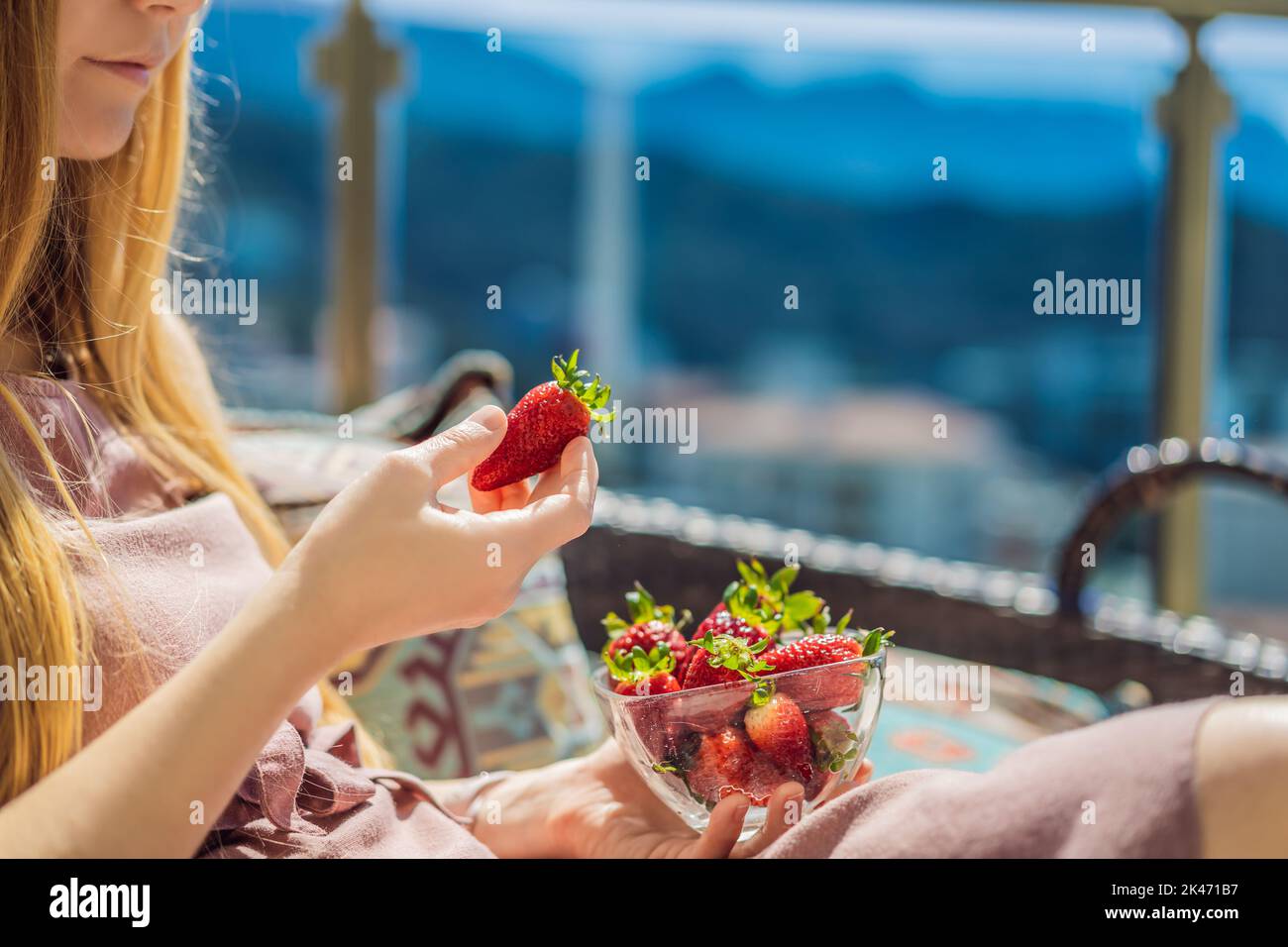 Portrait einer wunderschönen Frau in einem wunderschönen Kleid, die auf einer Terrasse sitzt und Erdbeere isst Stockfoto