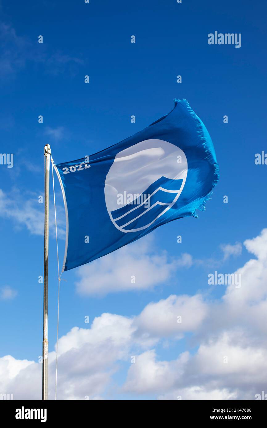 2022 Blaue Flagge Strand weht in der Brise gegen einen blauen Küstenhimmel Stockfoto