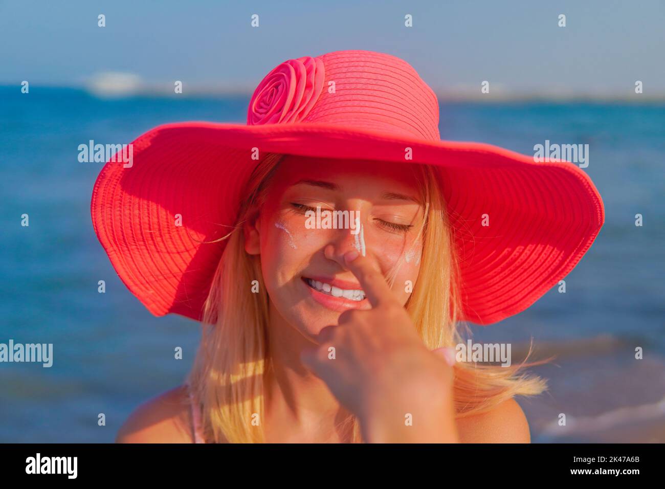 Teenager Mädchen in rosa Hut verbreiten Sonnencreme und lachen Stockfoto