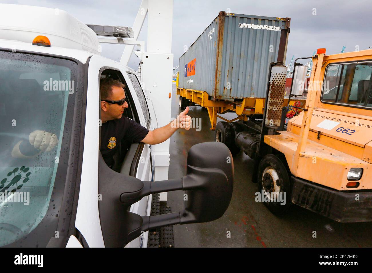 Ein US-Zoll- und Grenzschutzbeamter gibt dem Fahrer eines Lkw, der einen Transportcontainer zieht, die Daumen nach oben, nachdem er von LKW-montierten Strahlungserkennungssystemen im Hafen von Miami in Miami, Florida, gescannt wurde., 07. Dezember 2015. CBP-Foto von Glenn Fawcett Stockfoto