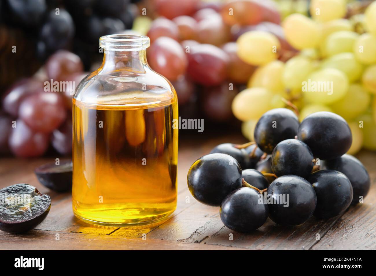 Flasche mit ätherischem Öl aus Bio-Traubenkernen. Schwarze, grüne und violette Trauben auf dem Tisch. Stockfoto