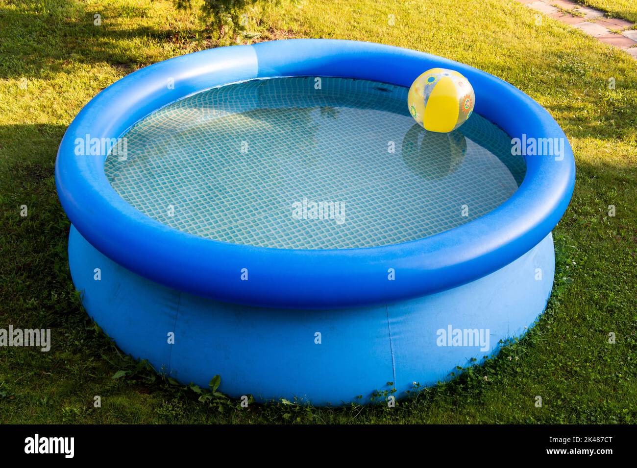 Eine gelbe Babykugel schwebt in einem blauen aufblasbaren Pool im Hinterhof. Stockfoto