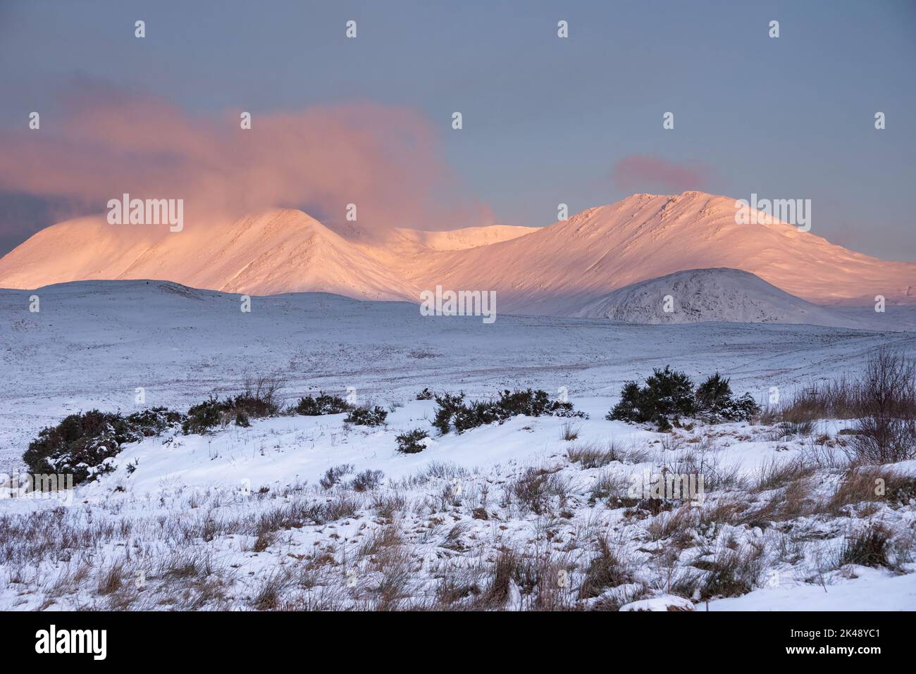 Wunderschöne Alpen Glow treffen Berggipfel in den schottischen Highlands während des atemberaubenden Sonnenaufgangs in der Winterlandschaft Stockfoto