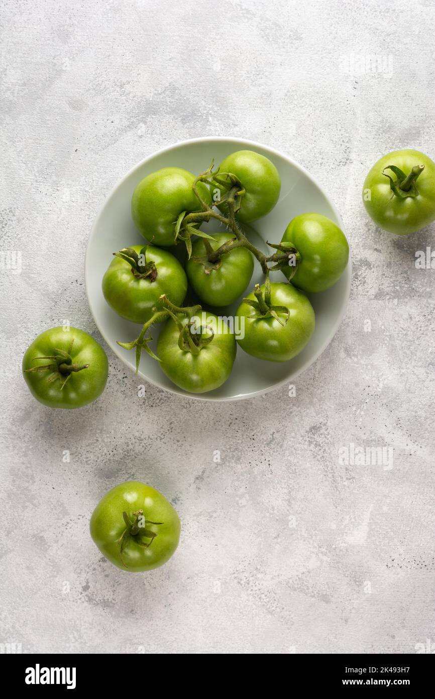 Tomaten auf einem weißen Teller, frisch geerntete grüne Beeren, verstreut auf einer strukturierten Tischplatte, von oben mit Platz für Kopien aufgenommen Stockfoto