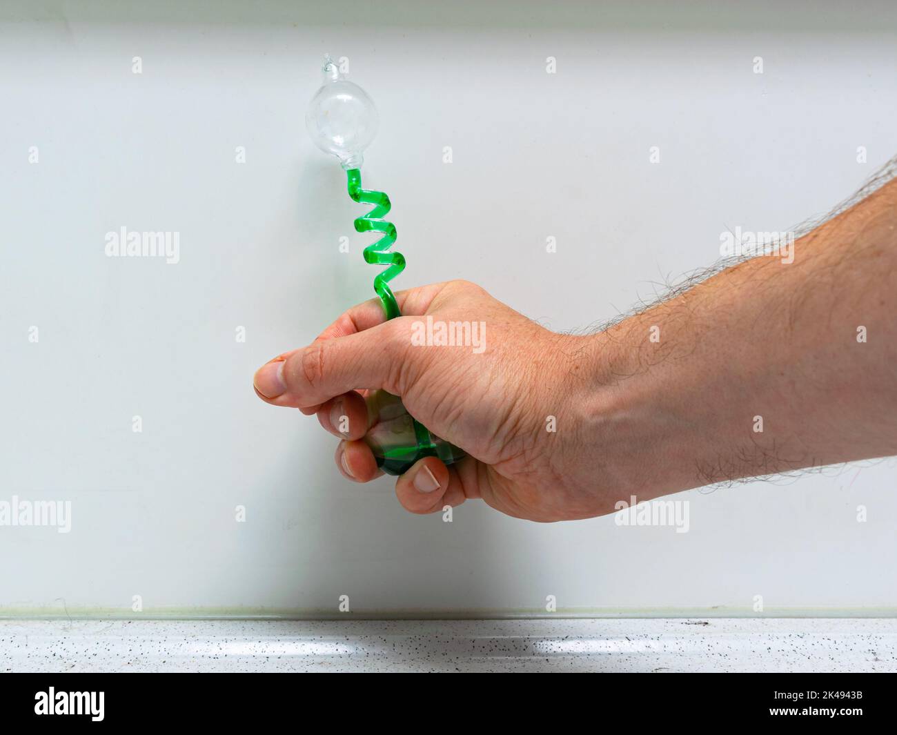Kleines Gerät, das anzeigt, dass sich die grüne Flüssigkeit ausdehnt, wenn Sie sie von Hand erhitzen. Wird als Demonstrationsmodell im Physikunterricht an der Schule verwendet. Stockfoto
