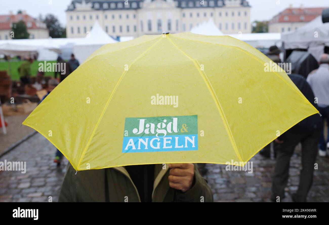 Wermsdorf, Deutschland. 01. Oktober 2022. Vor dem Schloss Wermsdorf trägt ein Besucher einen Regenschirm mit dem Logo der Messe „Jagd & Angeln“. Dort findet vom 01. Bis 03.10.2022 die größte Messe Ostdeutschlands zu den Themen Jagd, Fischerei und Outdoor statt. Die Show findet zum ersten Mal in diesem historischen Ambiente statt, zuvor fand sie in Markkleeberg bei Leipzig statt. Quelle: Sebastian Willnow/dpa/ZB/dpa/Alamy Live News Stockfoto