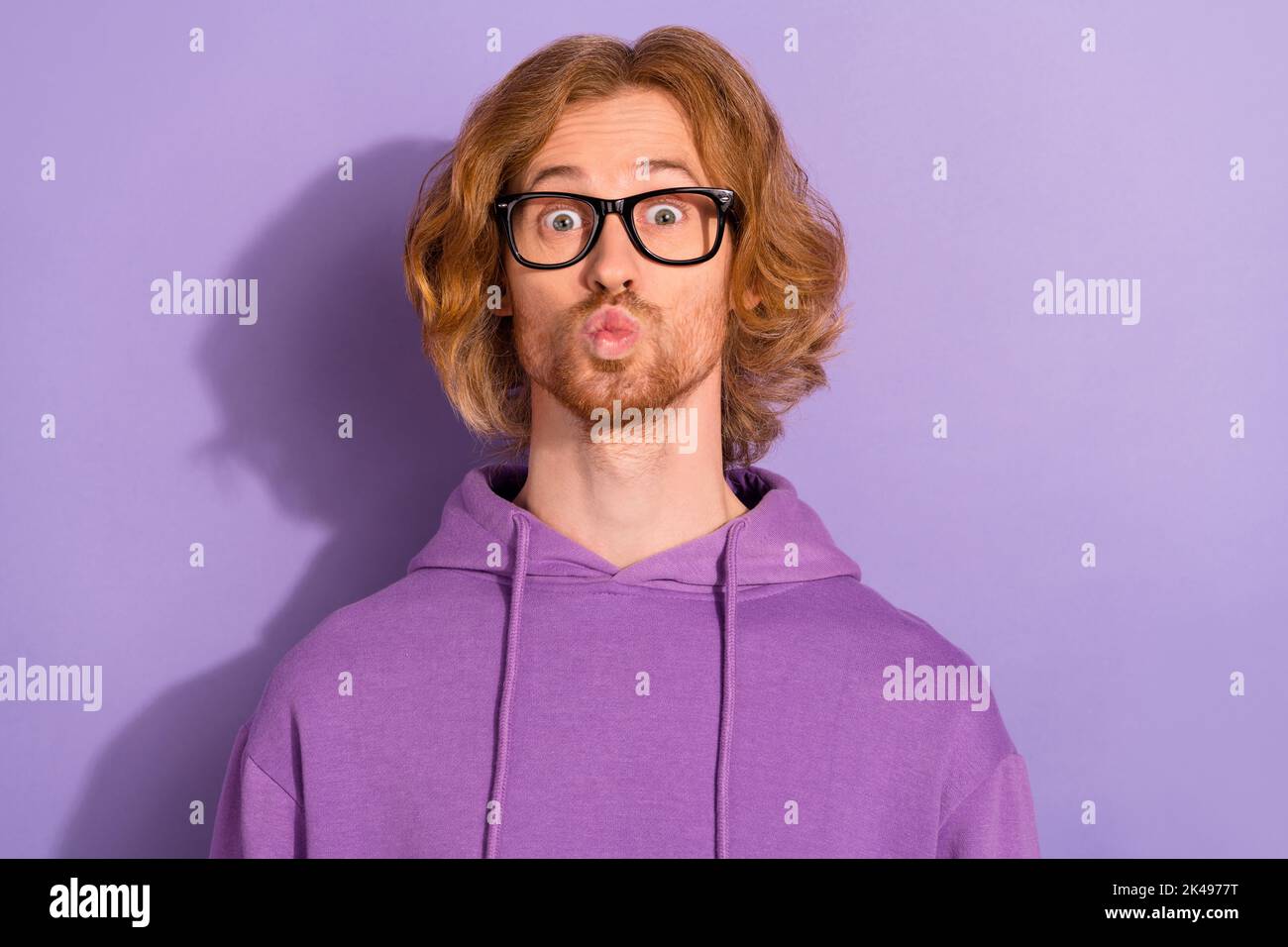 Foto von lustigen lockigen roten Frisur Kerl Schlag Kuss tragen Brillen lila Sporttuch isoliert auf violetten Hintergrund Stockfoto