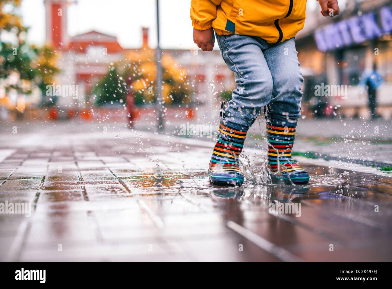 Glücklicher kleiner Junge, der in der Herbstsaison auf einer verregneten Pfütze in der Stadtstraße springt Stockfoto