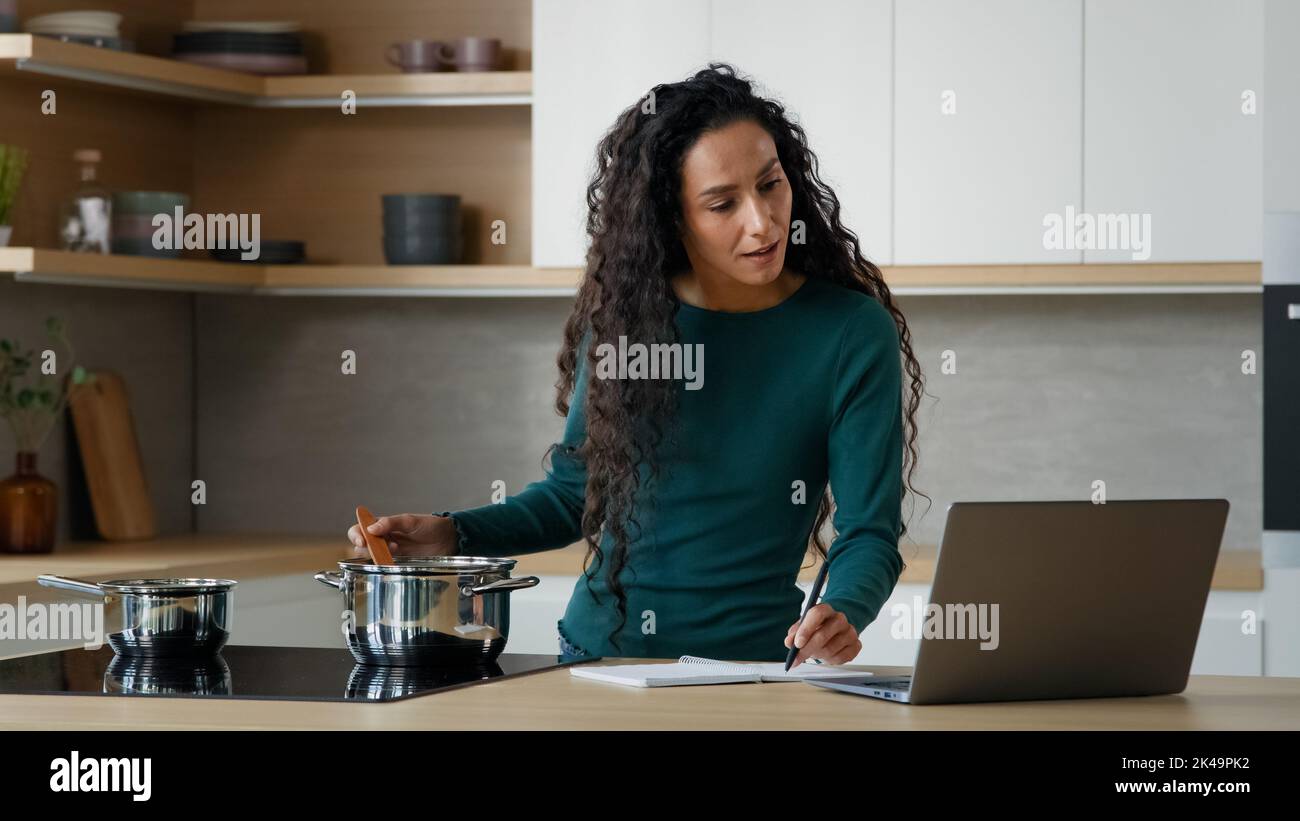 Arabische Frau Mutter Kochen Mittagessen Essen gesunde Lebensmittel in der modernen Küche Schreiben Internet Rezept mit hilfreichen Kochen Website auf Laptop-Kochbuch-Menü Stockfoto