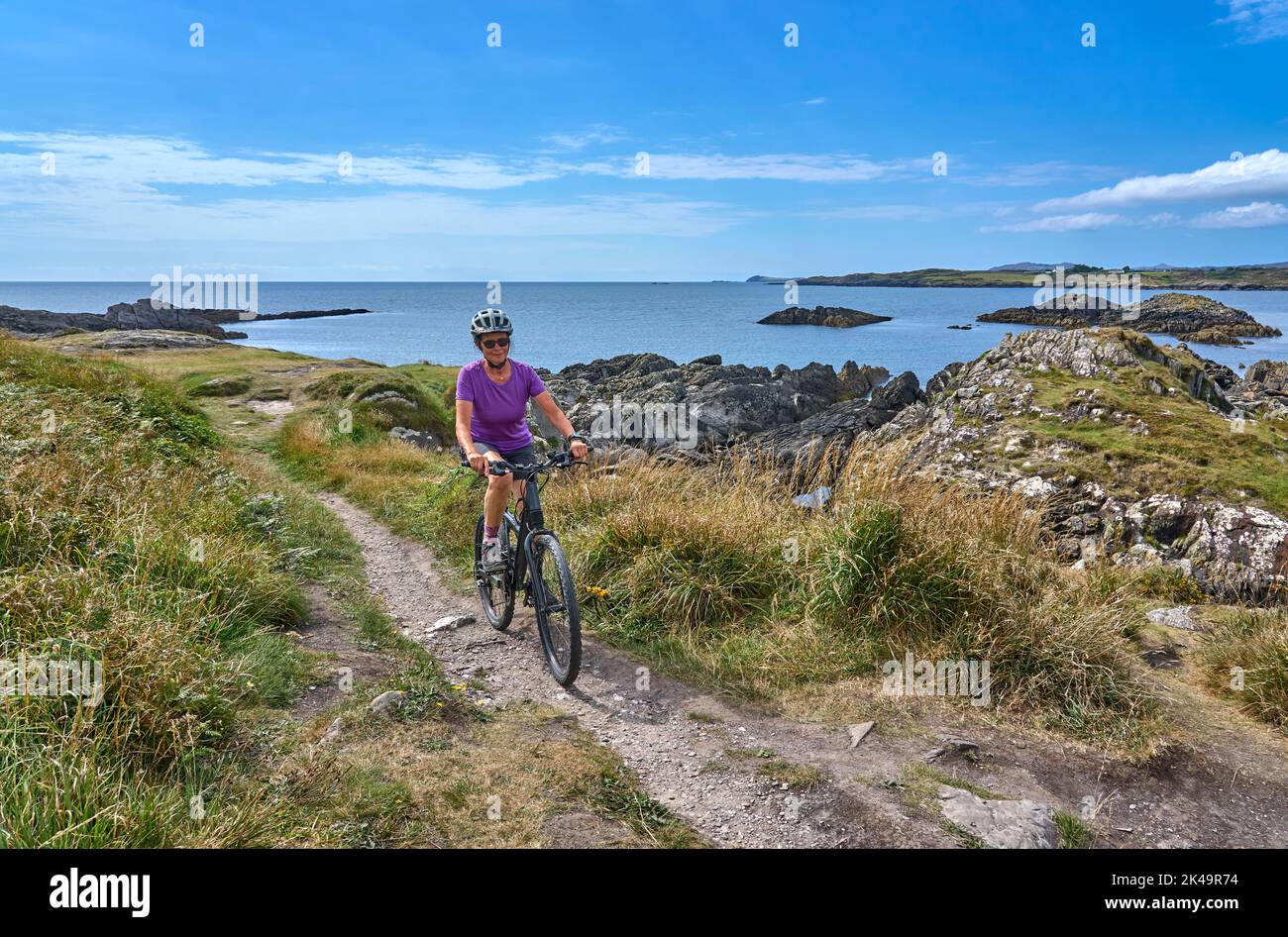 Nette ältere Frau auf dem Mountainbike, mit dem Fahrrad auf den Klippen von Toormore, Grafschaft Cork im Südwesten Irlands Stockfoto
