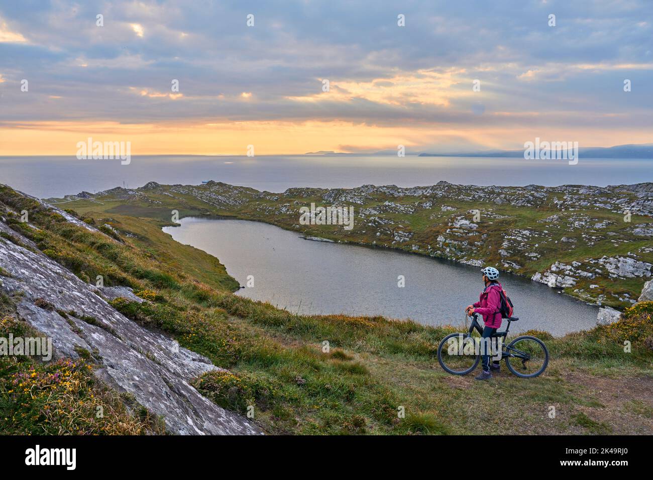 Nette ältere Frau auf dem Mountainbike, Radfahren und im Sonnenuntergang mit einem Schaf auf den Klippen von Sheeps Head, Grafschaft Cork, im südwestlichen Teil von t sprechen Stockfoto
