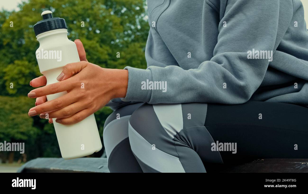 Nahaufnahme unbekannter Athlet gesunde Frau Läuferin trägt Sportanzug Sitzen Sie auf der Bank im Park Ruhe nach dem Training harte Workout-Übungen nehmen Pause Pause halten Stockfoto