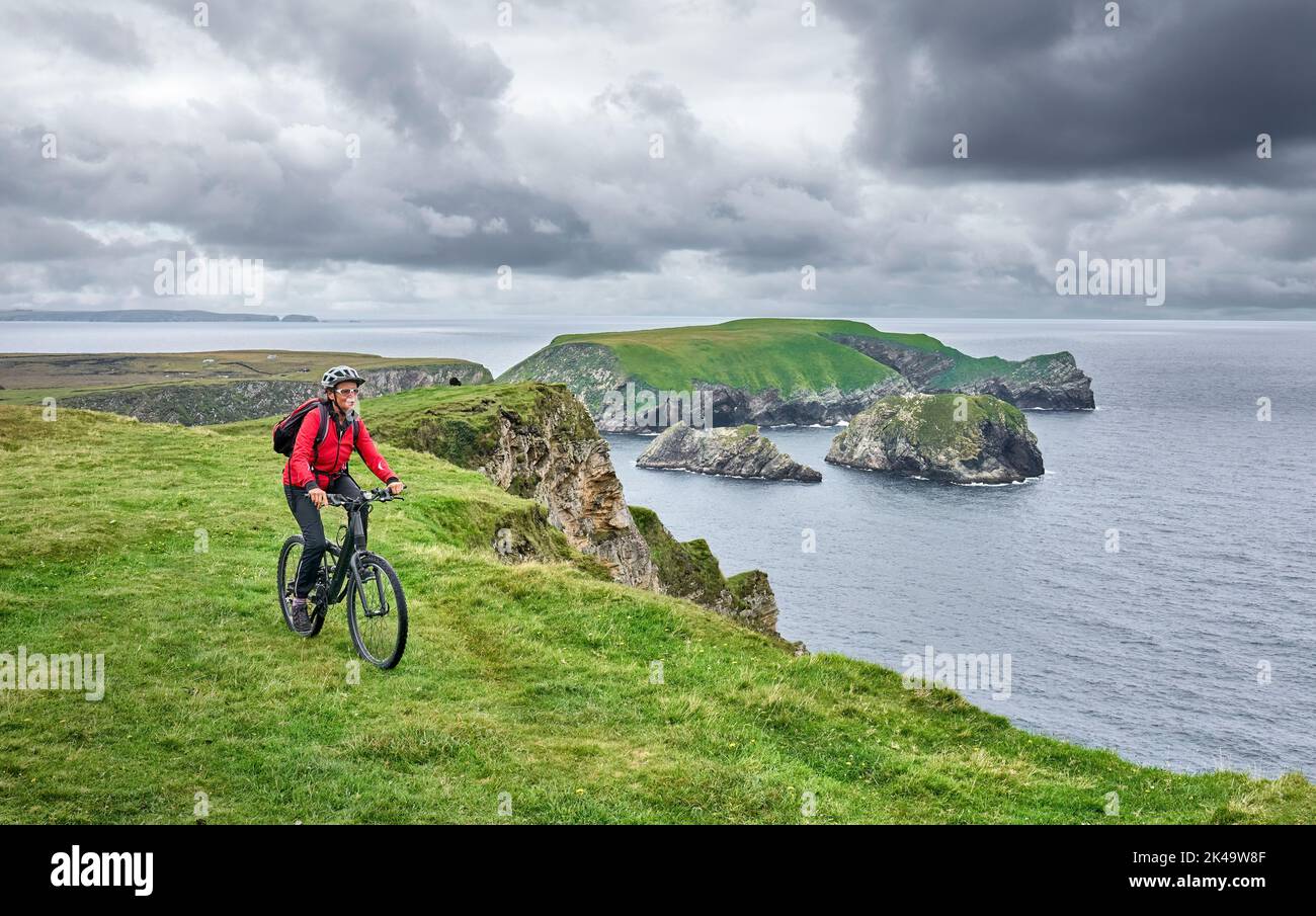 Nette ältere Frau auf dem Mountainbike, mit dem Fahrrad auf den Klippen von Cnoc an Daimh, Kilgalligan, dem nördlichen Teil der Republik Irland Stockfoto