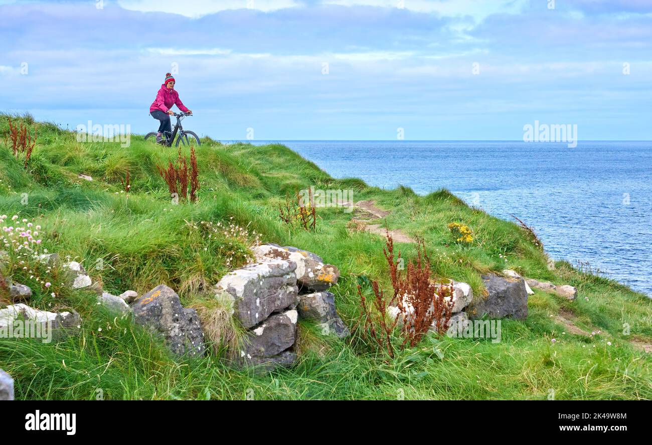 Nette ältere Frau auf dem Mountainbike, mit dem Fahrrad auf den Klippen von Cnoc an Daimh, Kilgalligan, dem nördlichen Teil der Republik Irland Stockfoto