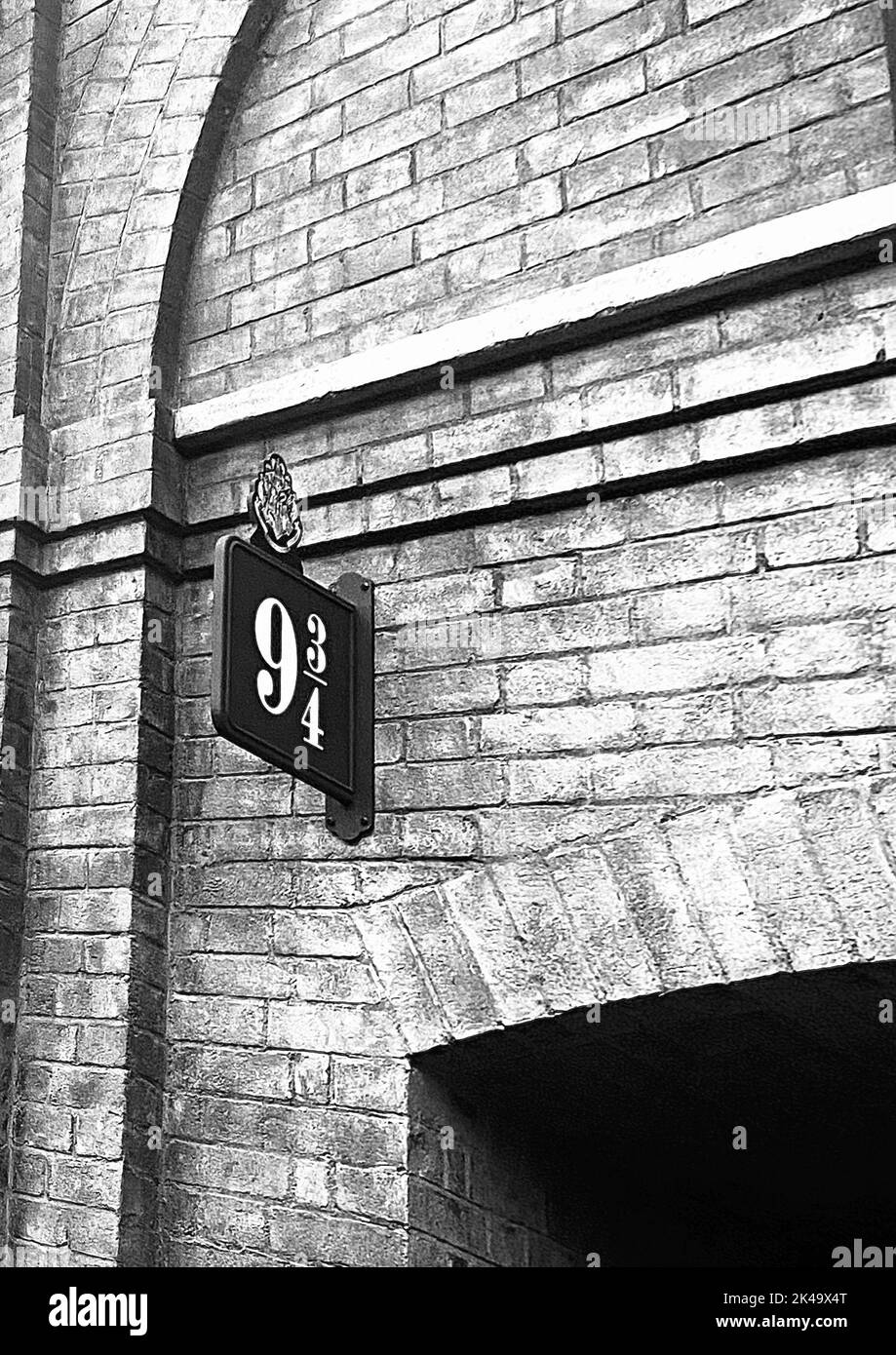 Die vertikale Graustufenansicht der Plattform 9 und drei Viertel Zeichen an der Steinmauer Stockfoto