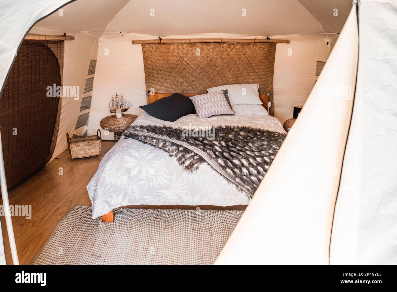 Gemütliches großes Bett im Zeltinneren mit Holzboden und grauen Teppichdecken Kissen und runden Nachttischen, tarawera See, Neuseeland Stockfoto