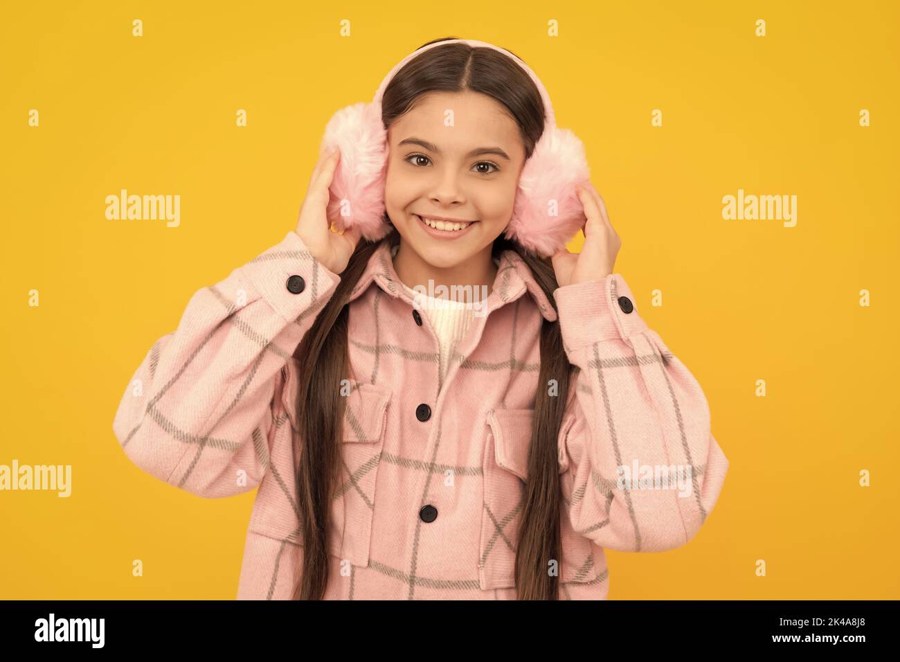 Happy Kid Lächeln in warmen Winterkleidung und Fell Ohrwärmer gelben Hintergrund, Ohrenschützer Stockfoto