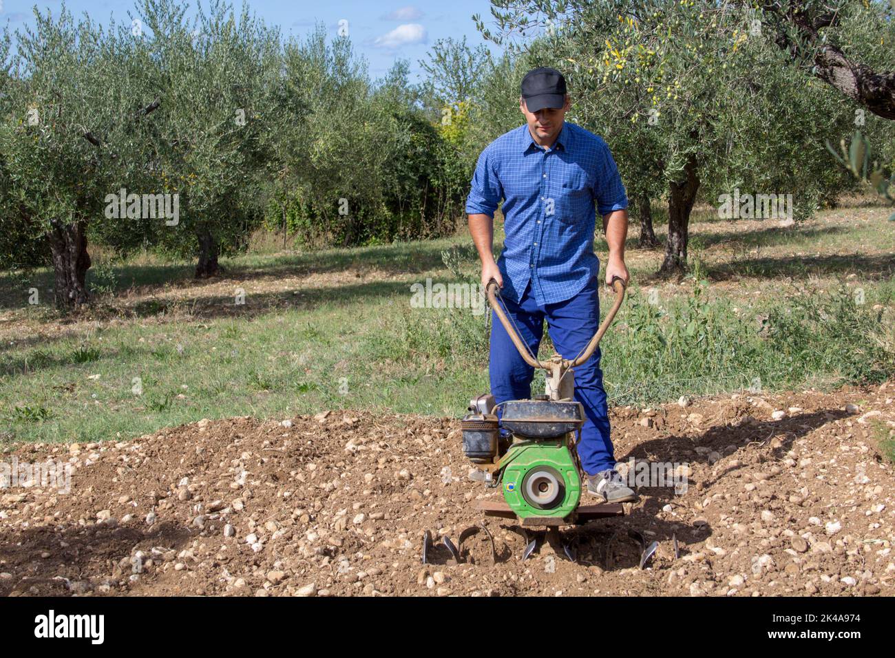 Bild eines Bauern, der mit einer Handfräse das Land für den Anbau seines Gemüsegartens vorbereitet. Stockfoto