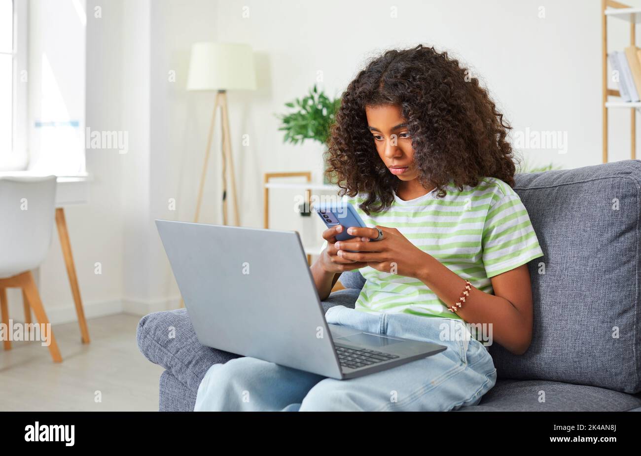 Afroamerikanisches Teenager-Mädchen, das süchtig nach ihrem Smartphone, Laptop und Social Media ist. Stockfoto