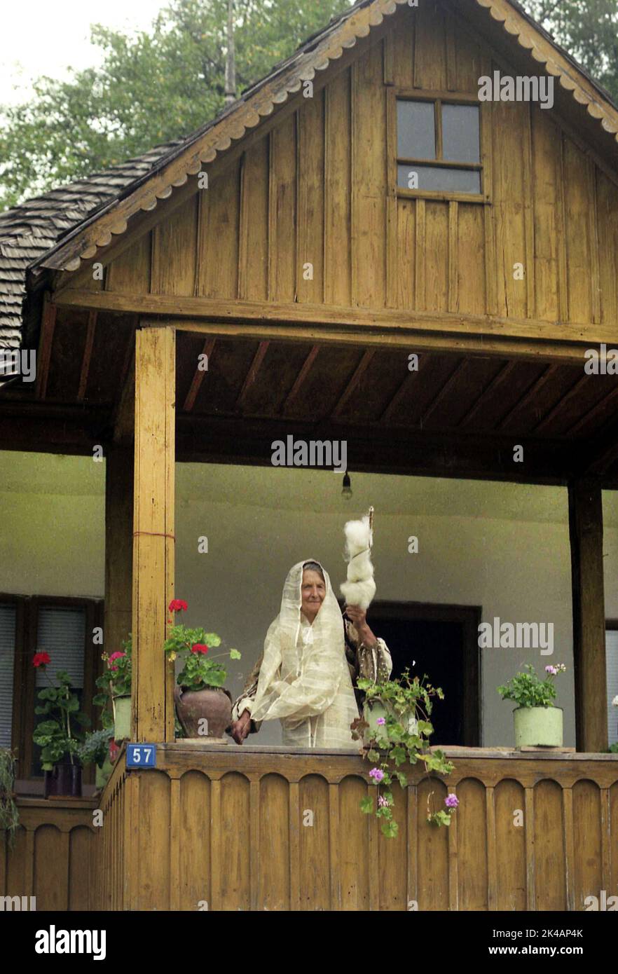 Nucsoara, Kreis Arges, Rumänien, ca. 2000. Ältere Frau auf der Veranda eines Holzhauses trägt eine traditionelle handgemachte Volkstracht und spinnt Wolle auf altmodische Weise. Stockfoto