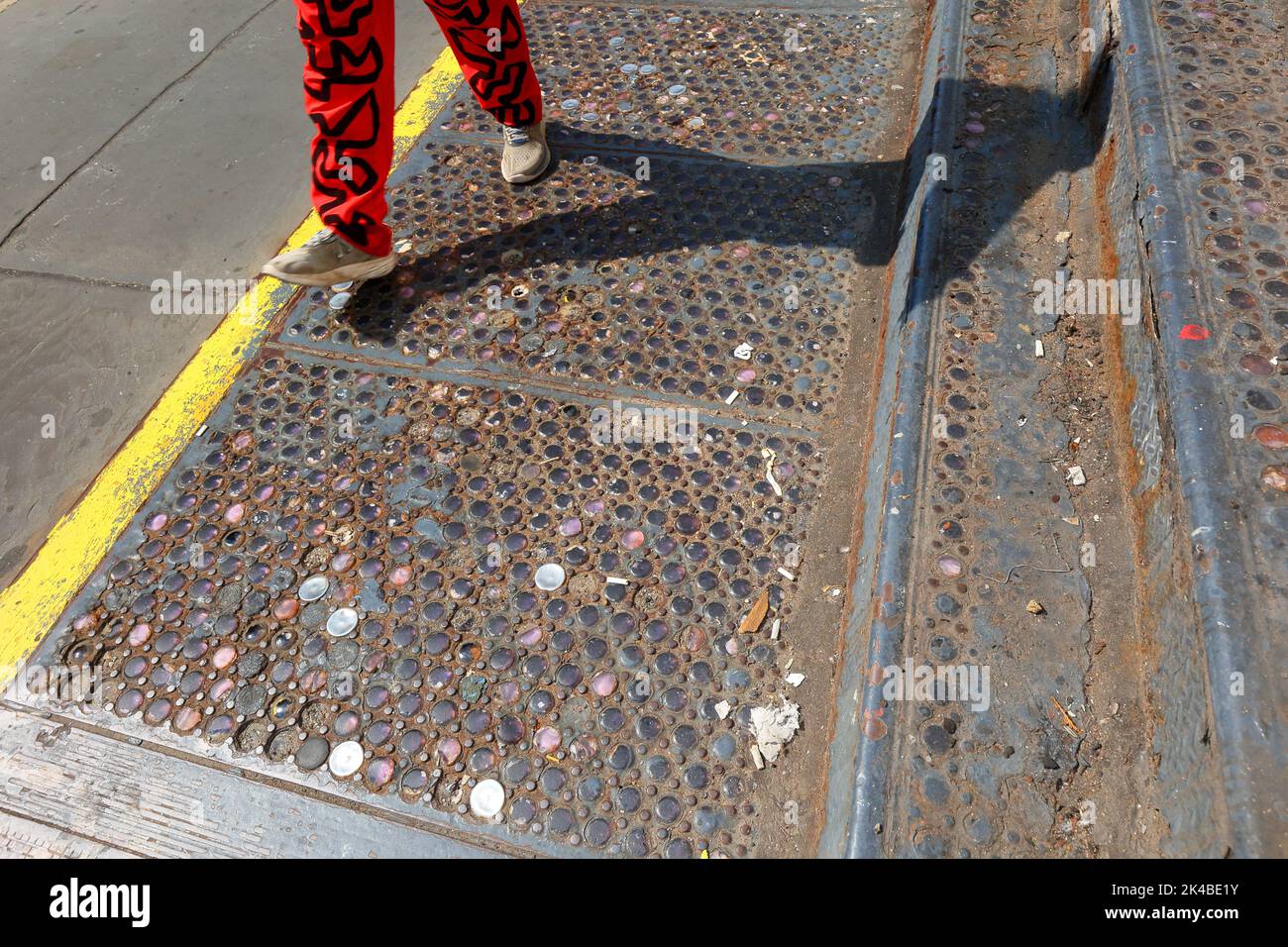 Eine Person geht über ein original gossenes Bürgersteigegewölbe aus New York City, eingebettet in farbenfrohe Glasperlen im Stadtteil SoHo in Manhattan. Stockfoto