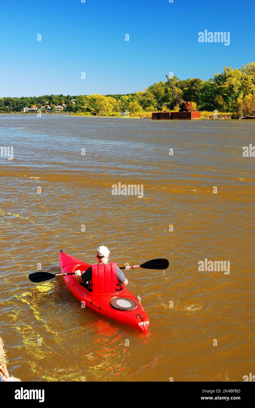 An einem sonnigen Sommerferientag fährt ein einsame Kajak auf einem ruhigen Nebenfluss zu einem großen Fluss Stockfoto