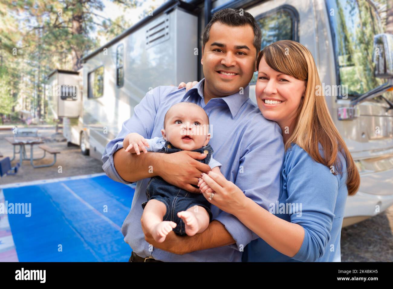 Glückliches multiethnisches kaukasisches und hispanisches Paar mit Baby vor ihrem schönen Wohnmobil auf dem Campingplatz. Stockfoto
