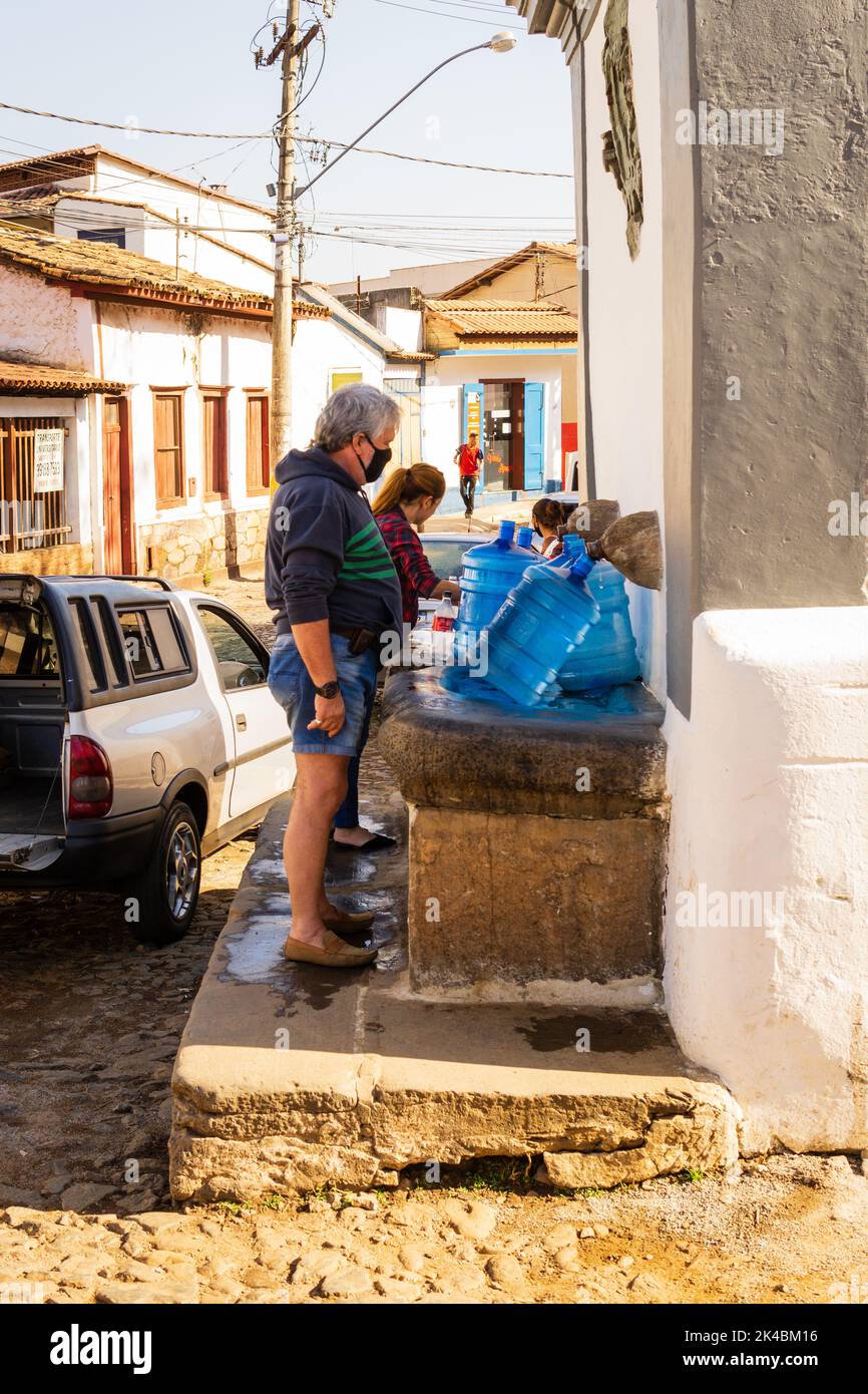 Menschen, die am Brunnen Chafariz do Kaquende in Sabará, Minas Gerais, Brasilien, blaue Wassergallonen mit Wasser füllen. Stockfoto