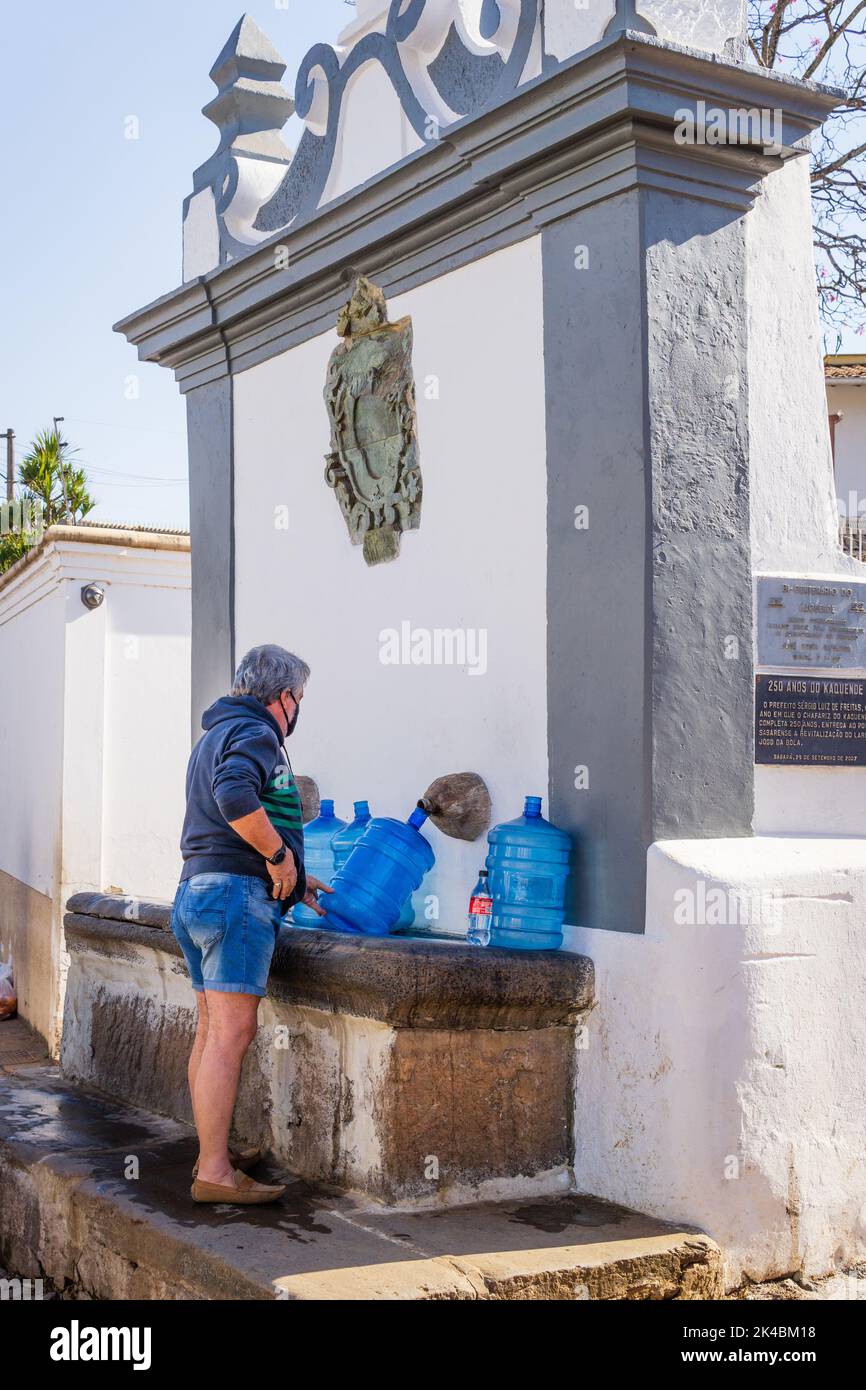 Mann, der am Brunnen Chafariz do Kaquende in Sabará, Minas Gerais, Brasilien, blaue Wassergallonen mit Wasser füllt. Stockfoto