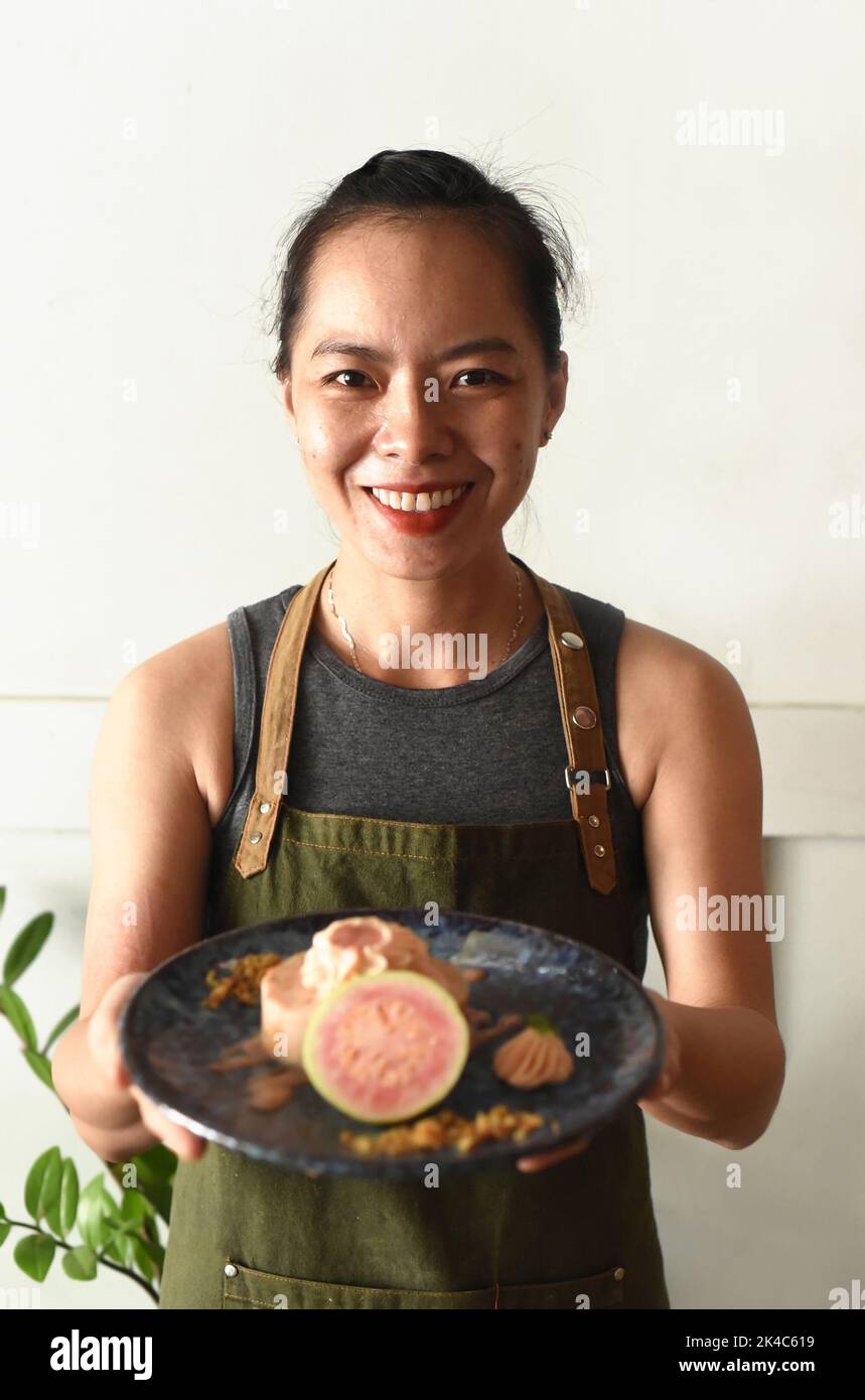 Vietnamesische Kellnerin lächelt und hält einen Teller mit Guava-Kuchen Stockfoto