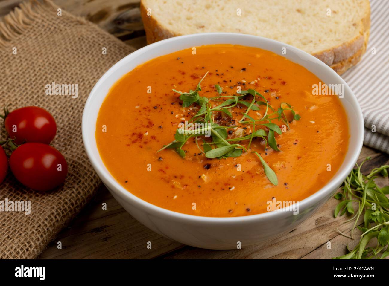 Horizontales Bild einer Schüssel Tomatensuppe mit Garnierung, Tomaten und Brotscheiben auf Holz Stockfoto