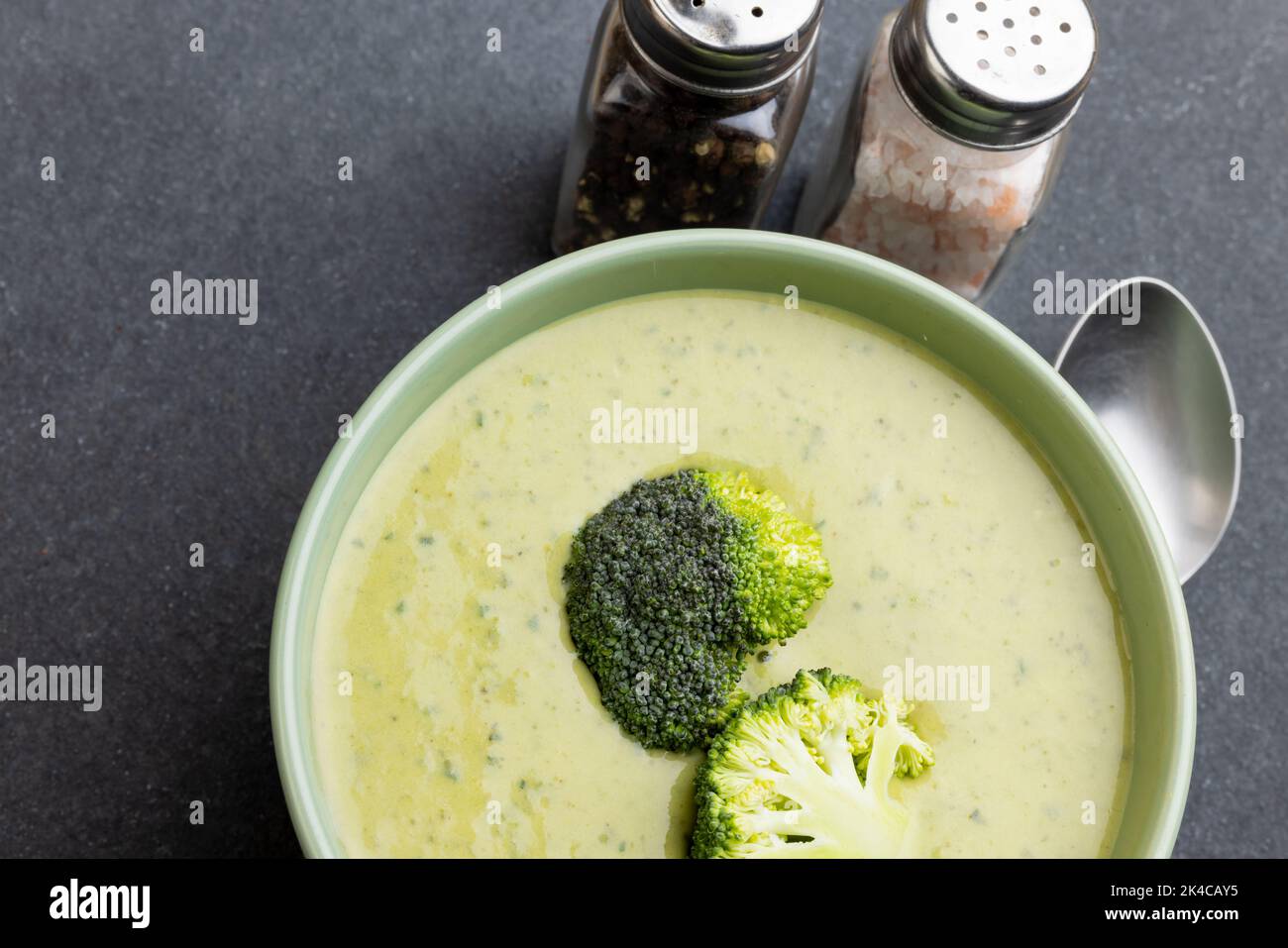 Horizontales Bild einer Schüssel mit Brokkoli-Suppe mit Röschen, Salz, Pfeffer, Löffel auf Schiefer, Kopierraum Stockfoto