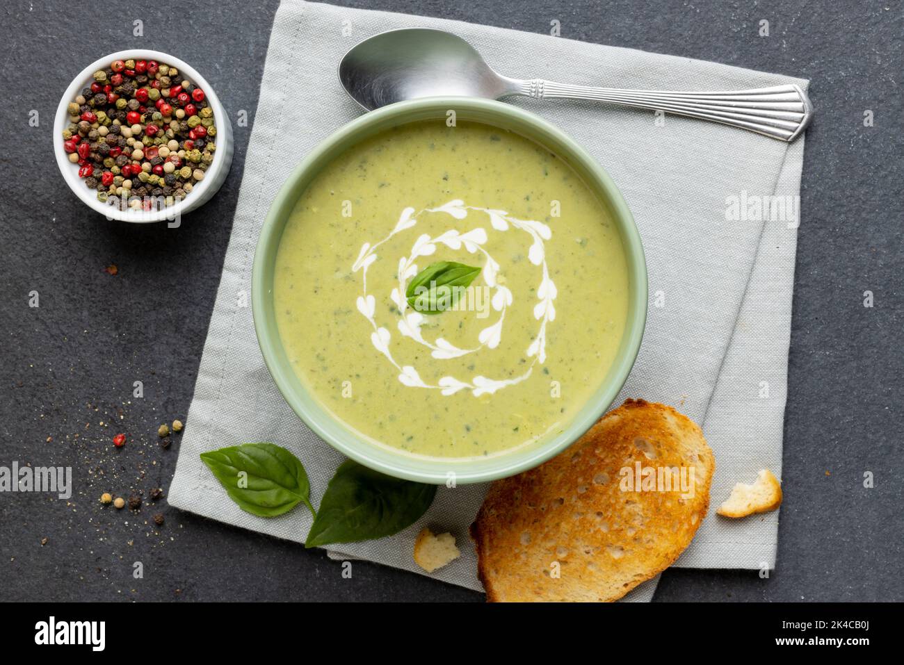 Horizontale Abbildung einer Schüssel Erbsensuppe mit Garnierung, mit Toast und Pfefferkörnern auf Schiefer Stockfoto