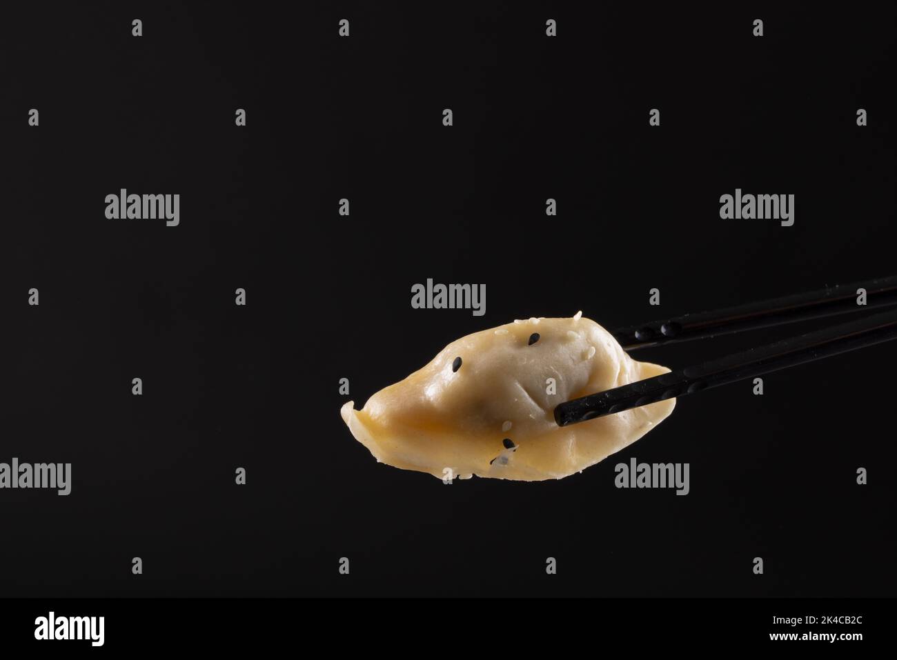 Ansicht des asiatischen Knödlers in schwarzen Stäbchen auf schwarzem Hintergrund Stockfoto
