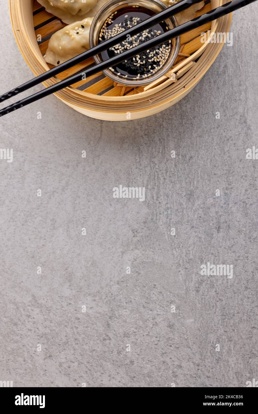 Blick von oben auf asiatische Knödel, Sojasauce und Essstäbchen in Holzschale auf grauem Hintergrund Stockfoto