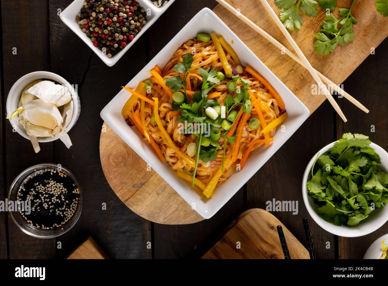 Blick von oben auf asiatische Wok-Rührgerichte mit Essstäbchen und Gewürzen auf Holzbrett Stockfoto