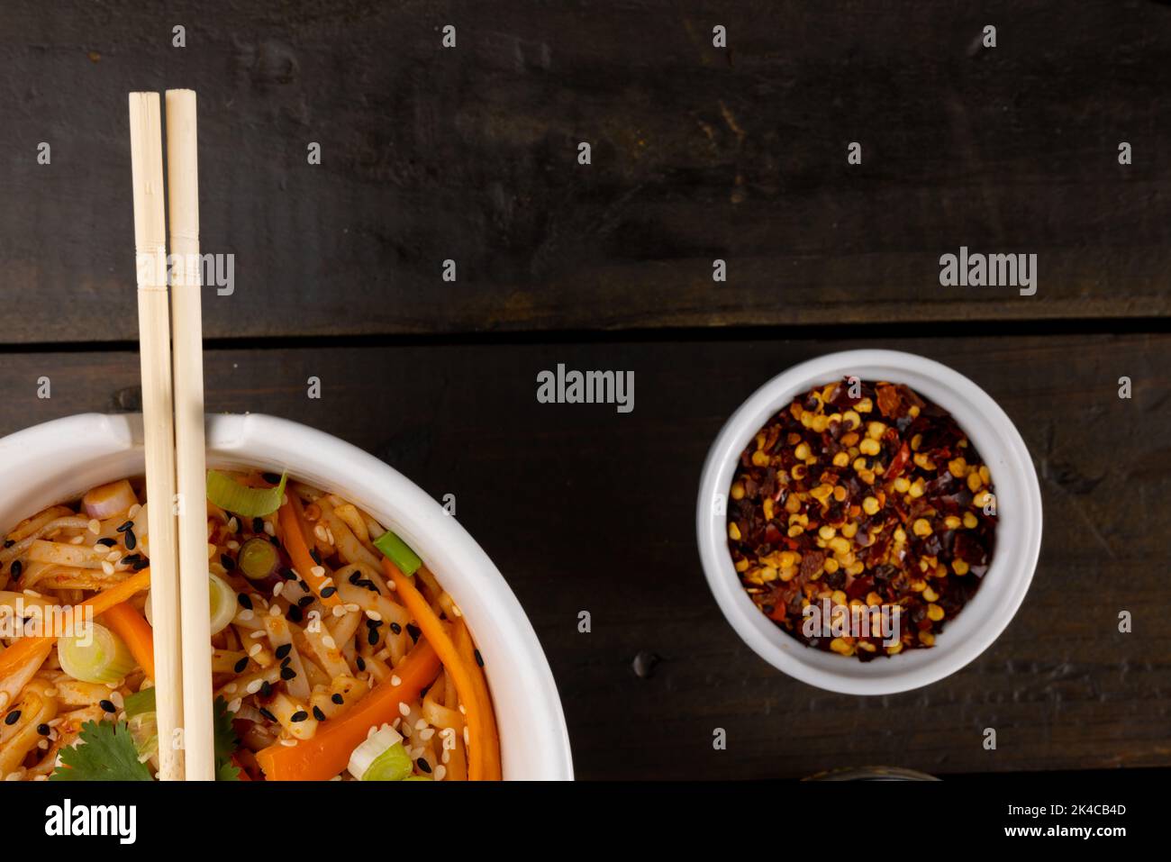 Blick von oben auf asiatische Wok-Rührgerichte, Essstäbchen und Gewürzen auf Holzhintergrund Stockfoto