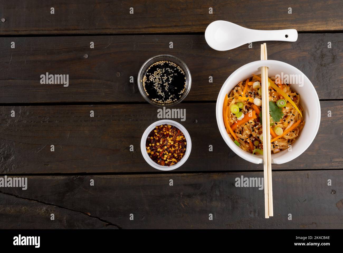 Blick von oben auf asiatische Wok-Rührgerichte, Essstäbchen und Gewürzen auf Holzhintergrund Stockfoto