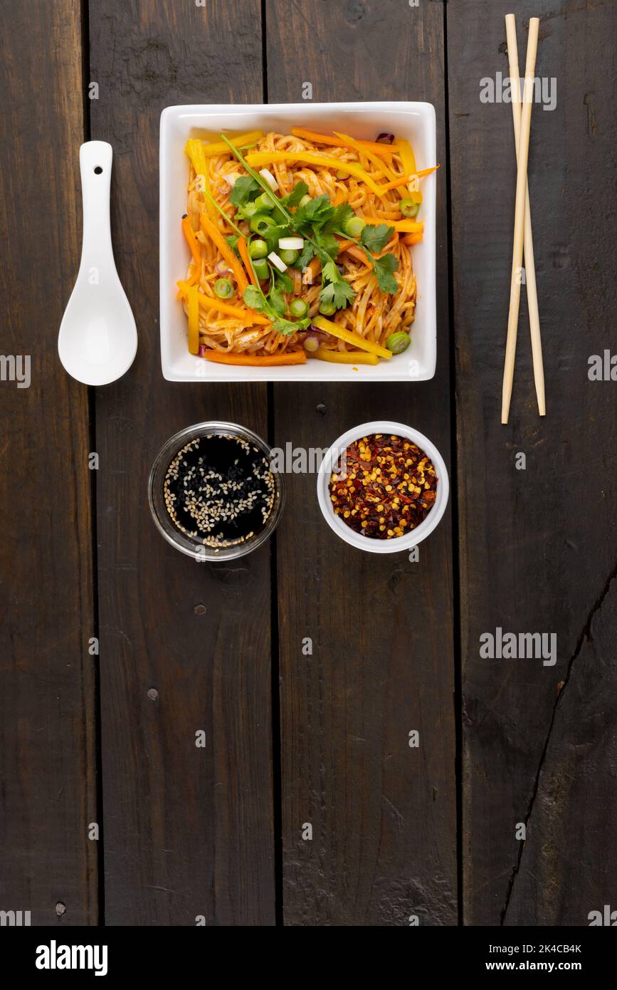 Blick von oben auf asiatische Wok rühren braten Nudeln und Essstäbchen, Löffel und Gewürze auf Holz Stockfoto