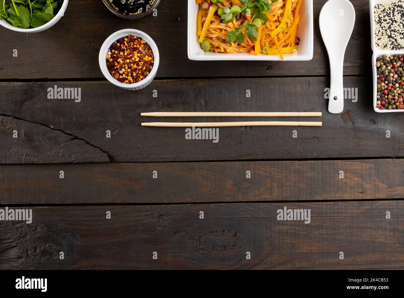 Blick von oben auf den asiatischen Wok, in dem Nudeln mit Essstäbchen, Löffel und Gewürzen auf Holz gebraten werden Stockfoto